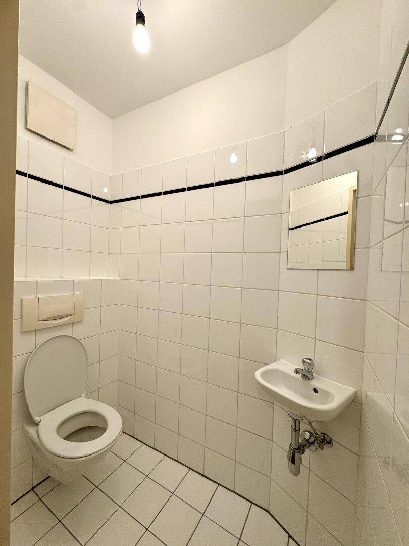 Separate Gästetoilette mit WC, kleinem Waschbecken und weißen Wand- und Bodenfliesen.