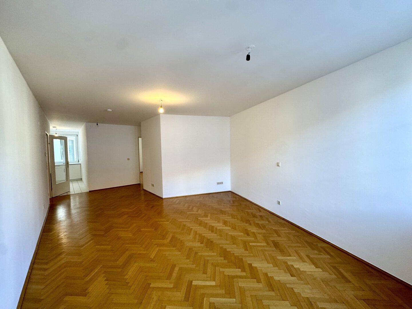 Geräumiges Wohnzimmer mit klassischem Fischgrätparkett und viel Tageslicht, ideal für neue Einrichtung.