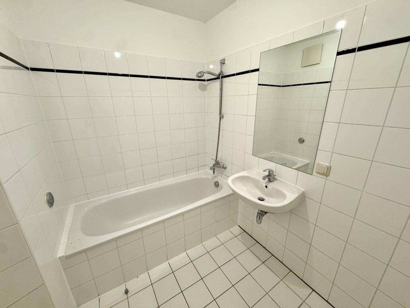 Badezimmer mit Badewanne, Waschbecken und weißen Fliesen, klassisch und funktional gestaltet.