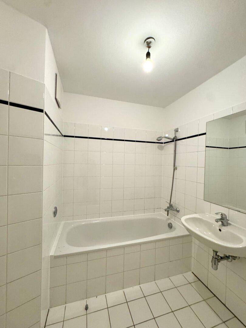 Funktionales Badezimmer mit Badewanne und Waschbecken, komplett gefliest in Weiß mit schwarzem Akzent.