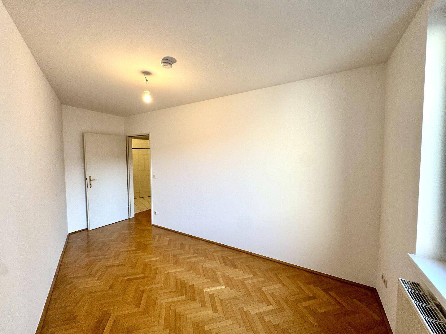 Unmöbliertes Zimmer mit Fischgrätparkett und weißer Wandfarbe, ideal für Schlaf- oder Arbeitsbereich.