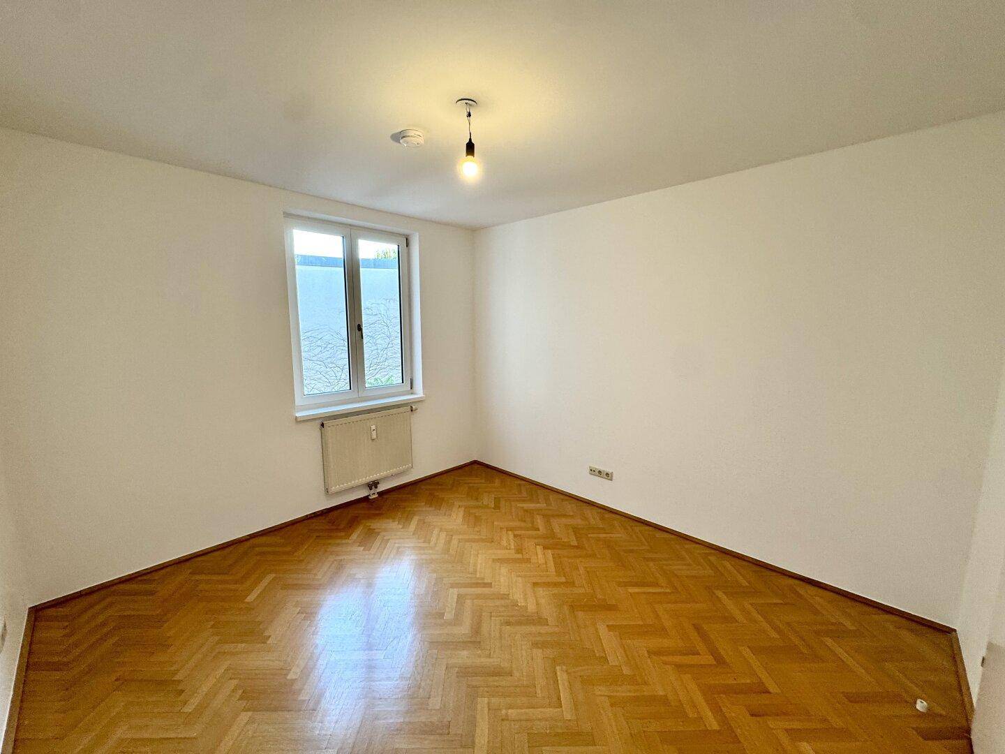 Ruhiges Zimmer mit Fischgrätparkett und einem Fenster, das viel natürliches Licht hereinlässt.