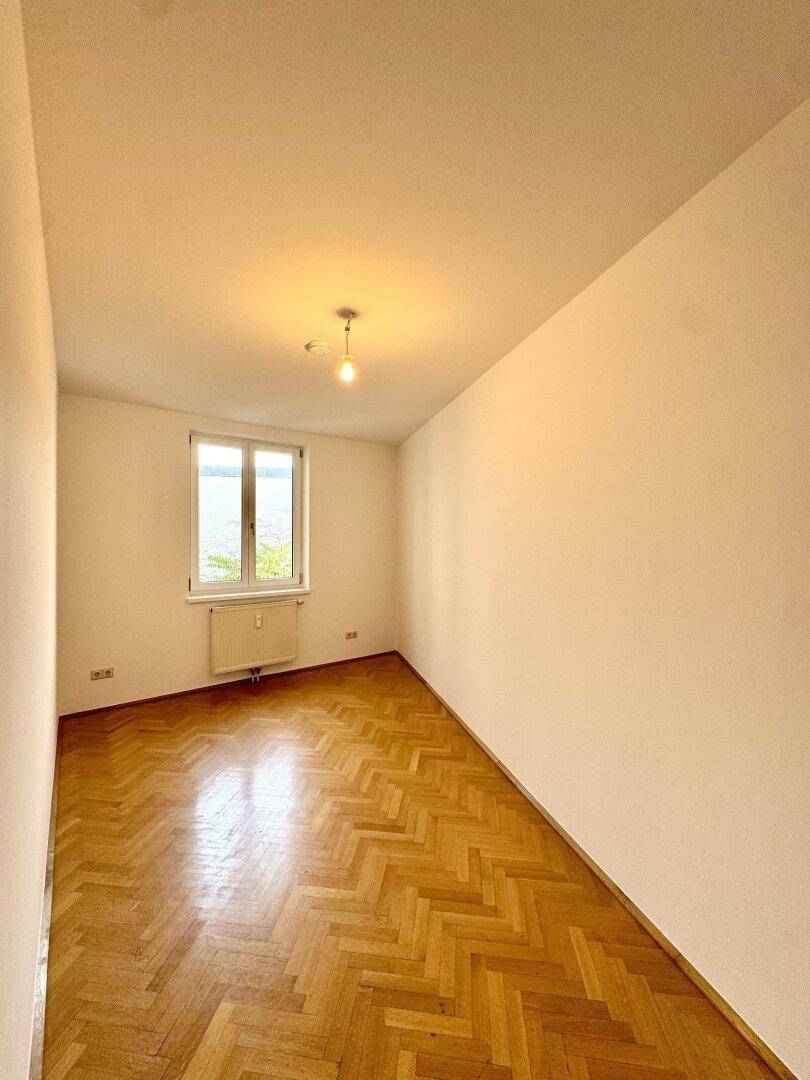 Helles Zimmer mit Fischgrätparkett und einem Fenster, das eine angenehme Atmosphäre schafft.