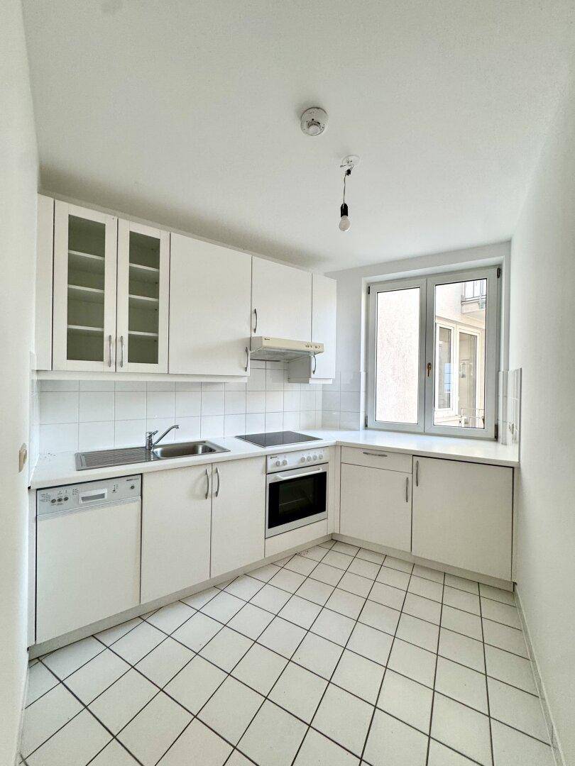 Funktionale Küche mit weißen Schränken, Elektrogeräten und einem Fenster für Tageslicht.