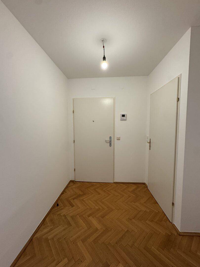 Heller Flur mit Fischgrätparkett und zwei Türen, der die verschiedenen Räume verbindet.