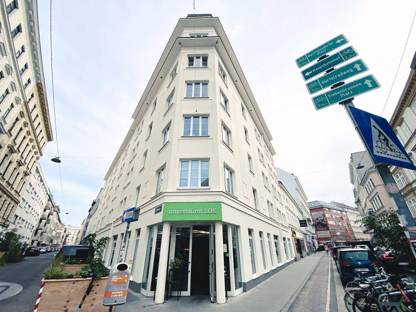 Modernes Eckgebäude mit großen Fenstern und einem Geschäft im Erdgeschoss an einer Stadtstraße.
