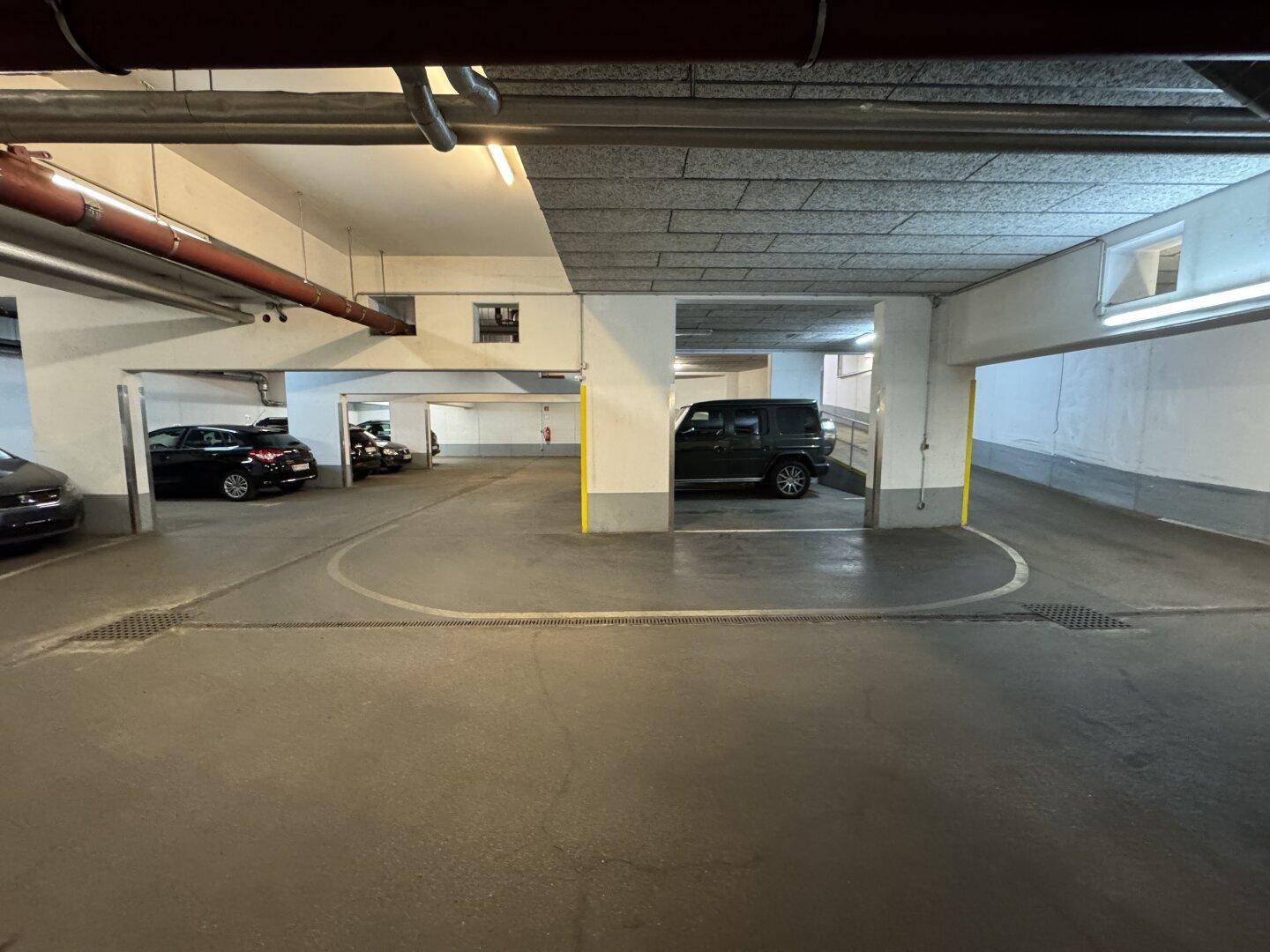Geräumige Tiefgarage mit Zufahrtsrampe und weiteren Parkplätzen im Hintergrund.