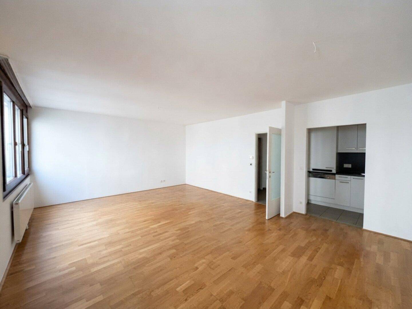 Großer Wohnbereich mit Parkettboden und Zugang zu einer kleinen, separaten Küche.