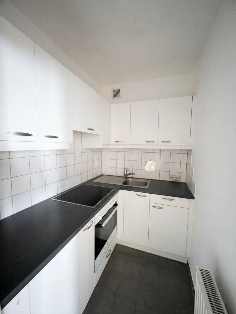 Funktionale, schmale Küche mit weißen Schränken, dunkler Arbeitsplatte und Fliesen-Rückwand.