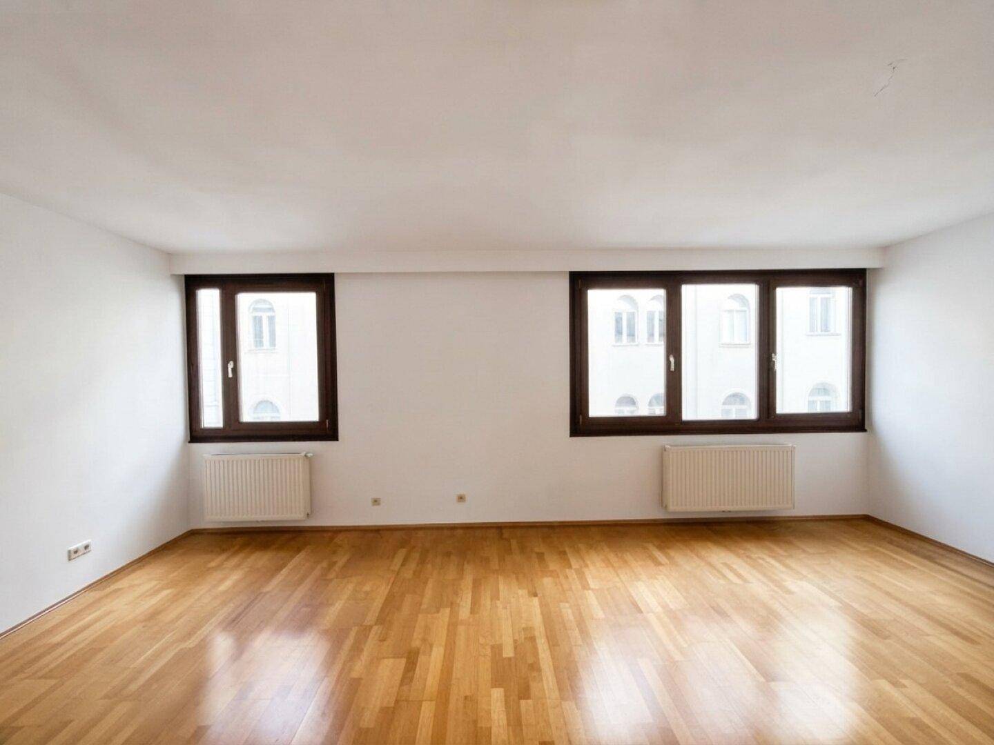 Heller Raum mit zwei großen Fenstern und Parkettboden, ideal für Wohn- oder Schlafzimmernutzung.