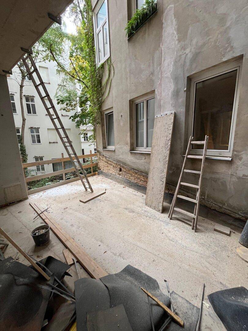 Baustelle einer zukünftigen Terrasse mit Blick auf den Innenhof und angrenzende Gebäude.