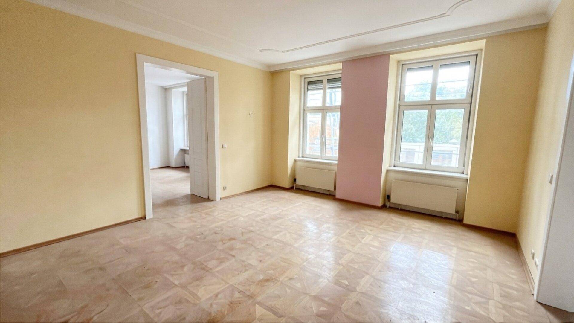 Geräumiges Wohnzimmer in einem Altbau mit Fischgrätparkett und Stuckdecke, bereit zur Renovierung.
