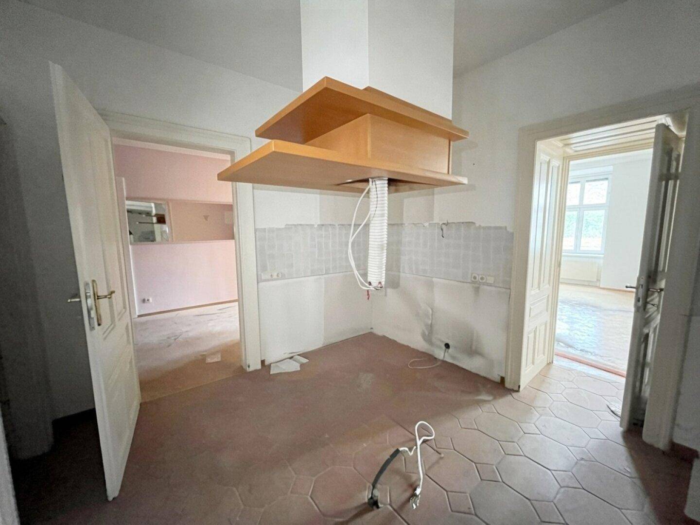 Leere Küche in einem Altbau mit Fliesenboden und vorbereiteter Dunstabzugshaube, renovierungsbedürftig.