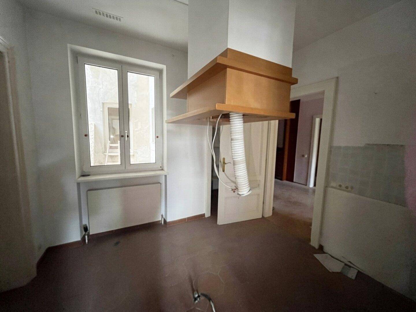 Leere Küche in einem Altbau mit Fliesenboden und vorbereiteter Dunstabzugshaube, renovierungsbedürftig.