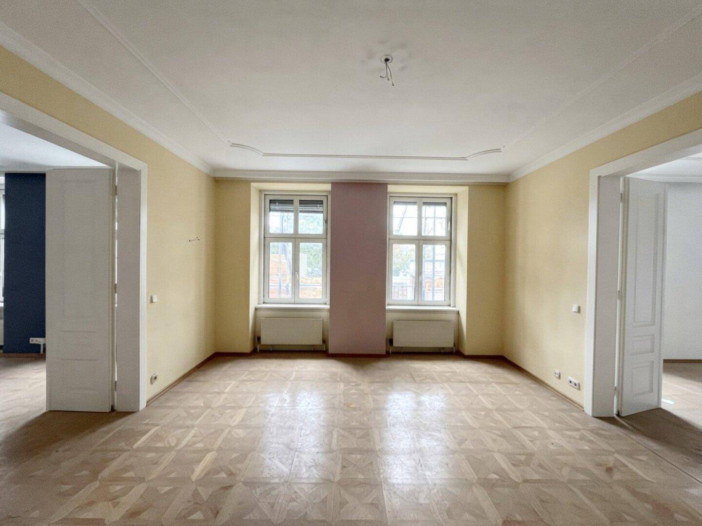 Geräumiges Wohnzimmer in einem Altbau mit Fischgrätparkett und Stuckdecke, bereit zur Renovierung.