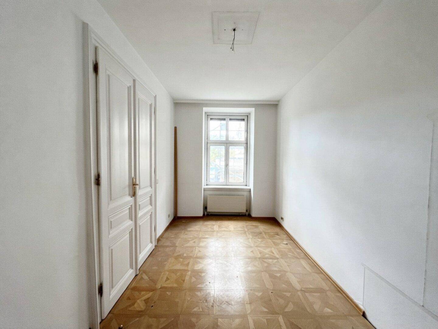 Helles Schlafzimmer in einem Altbau mit Fischgrätparkett und hohen Flügeltüren, renovierungsbedürftig.