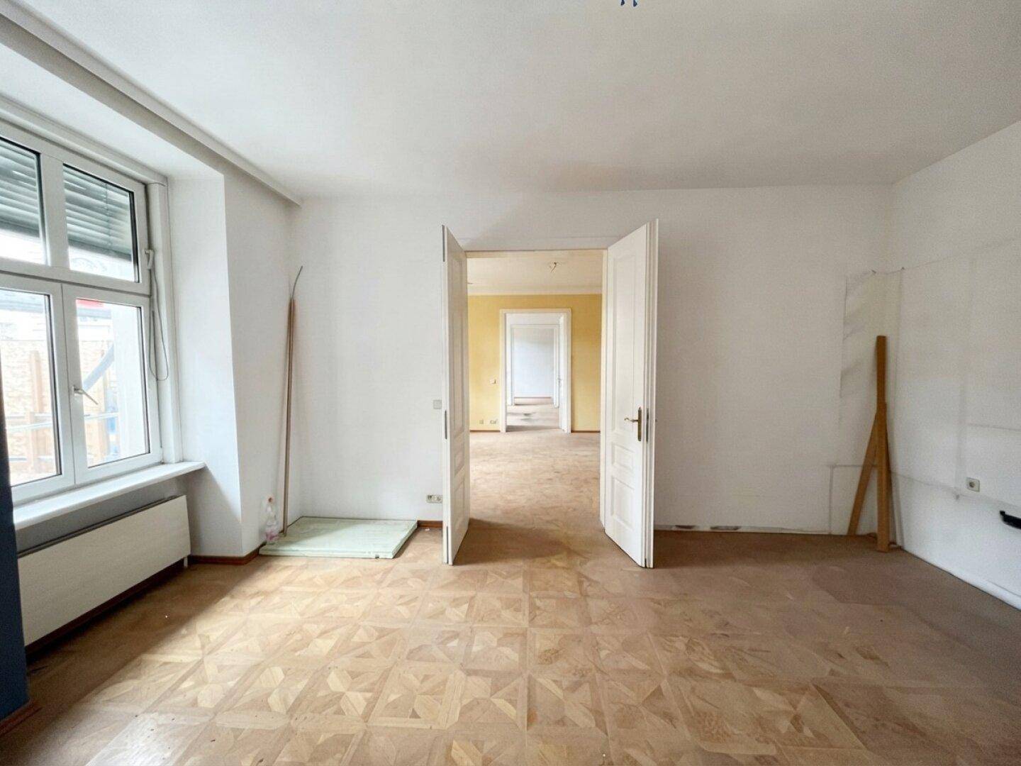 Helles Wohnzimmer in einem Altbau mit Fischgrätparkett und Blick in angrenzende Räume.
