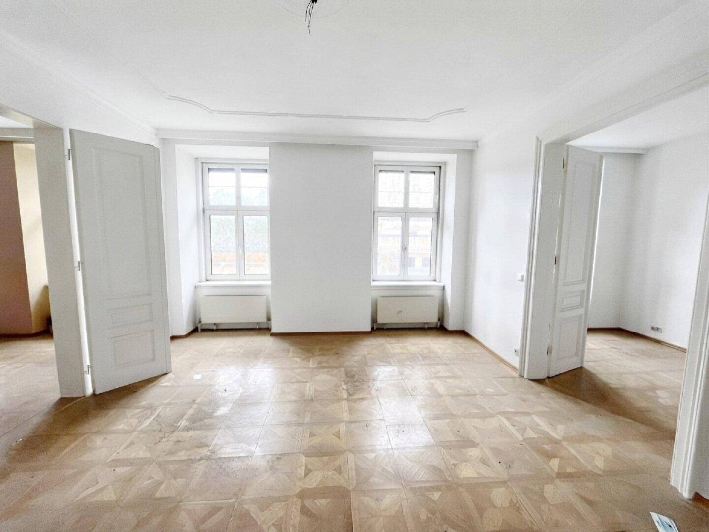 Geräumiges Wohnzimmer in einem Altbau mit Fischgrätparkett und Stuckdecke, bereit zur Renovierung.
