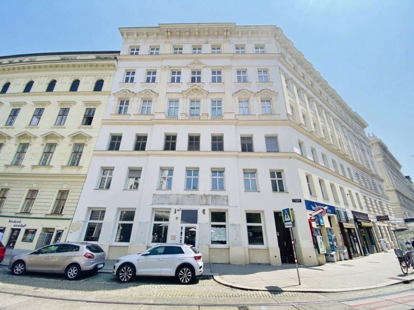 Historisches Eckgebäude in der Stadt mit klassischer Architektur und Geschäften im Erdgeschoss.