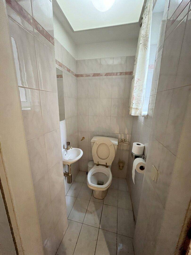 Kleines Gäste-WC mit Toilette, Handwaschbecken und Fenster, funktional und hell.