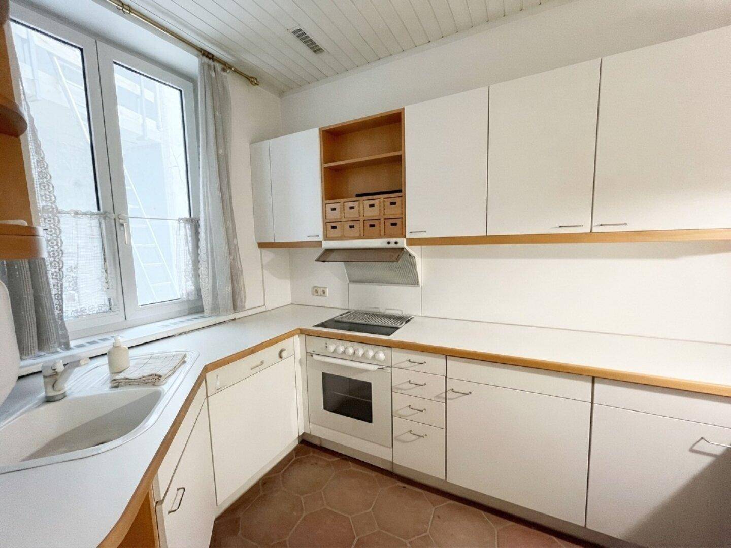 Funktionale Küche mit weißen Schränken, Holzdetails, Einbauherd und Fenster über der Spüle.