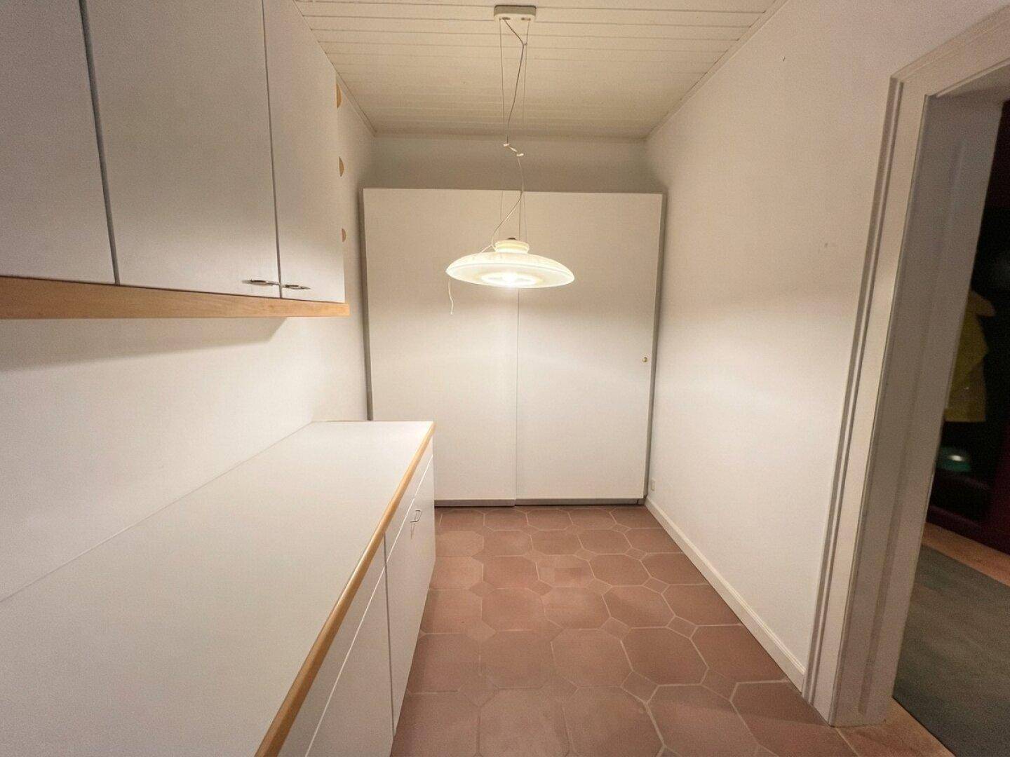 Praktischer Bereich mit weißen Schränken, Terrakotta-Fliesenboden und großem Einbauschrank für Stauraum.