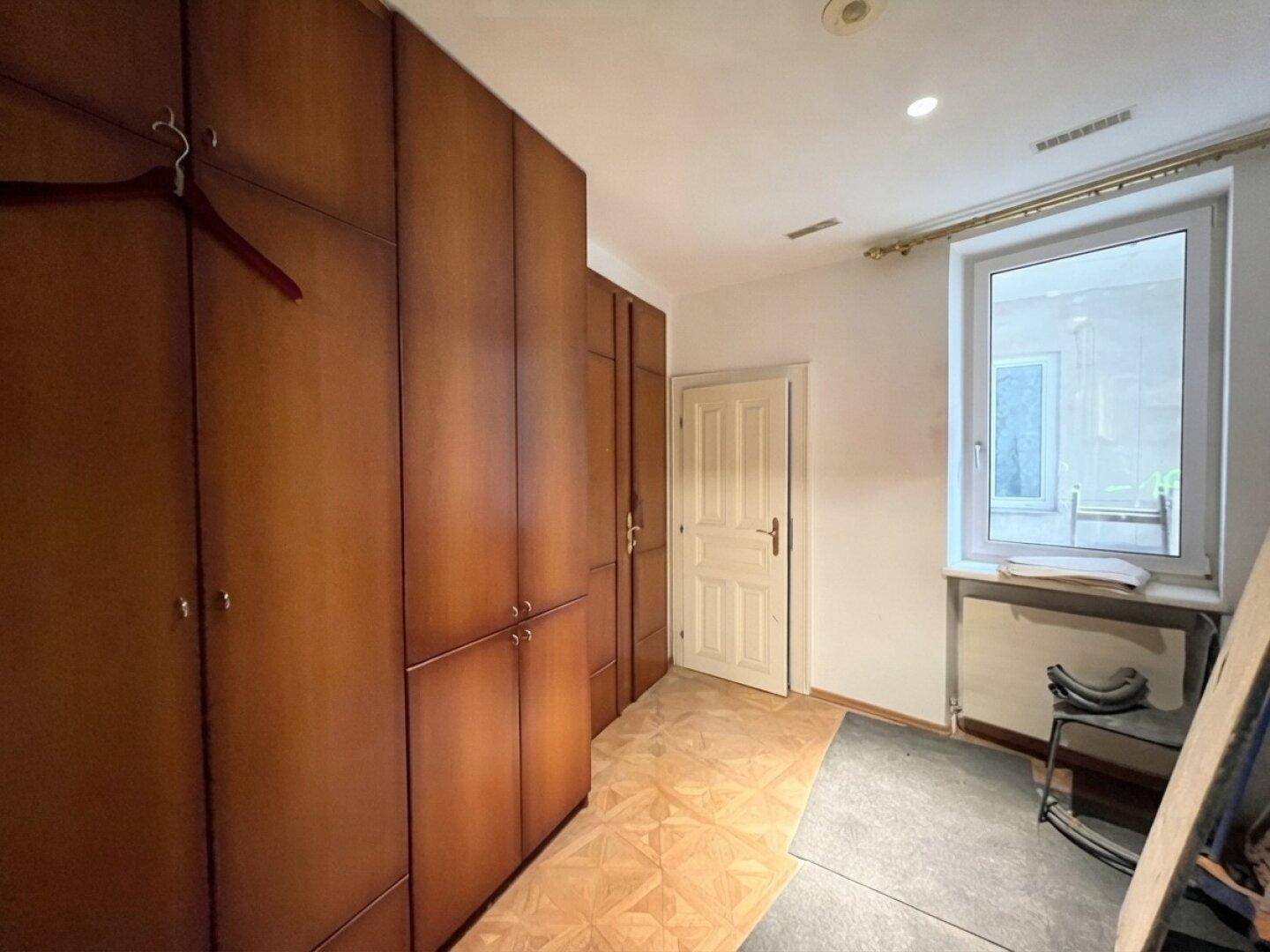Heller Flur mit Holz-Einbauschränken, Parkettboden und einem Fenster, das Tageslicht spendet.