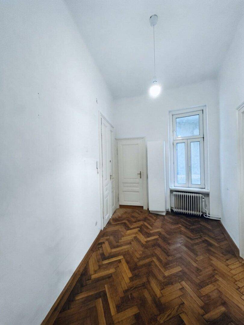 Langer Flur mit Fischgrätparkett, Fenster und mehreren Türen.