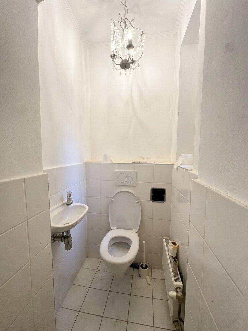 Kleines Gäste-WC mit Toilette, Waschbecken und dekorativem Kronleuchter.