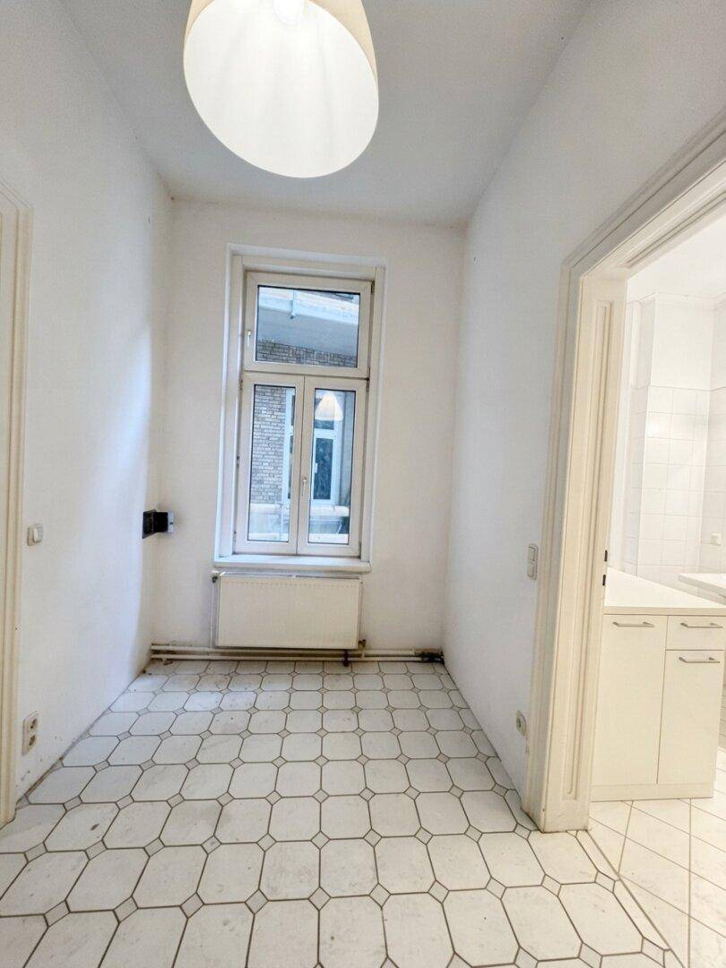 Kleiner Raum mit Fenster, gefliestem Boden und Zugang zur Küche.