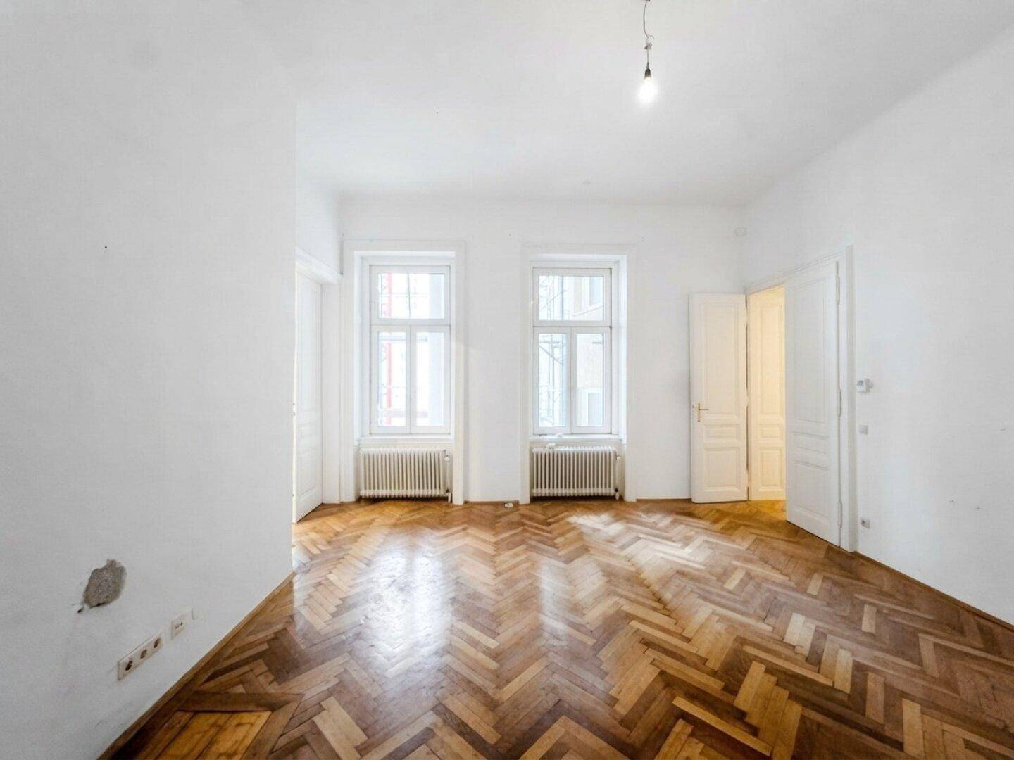Helles Zimmer mit zwei Fenstern, Fischgrätparkett und hohen Decken.