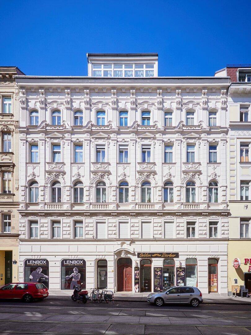 Elegante Altbaufassade mit Stuckverzierungen und modernen Dachaufbauten in der Stadt.