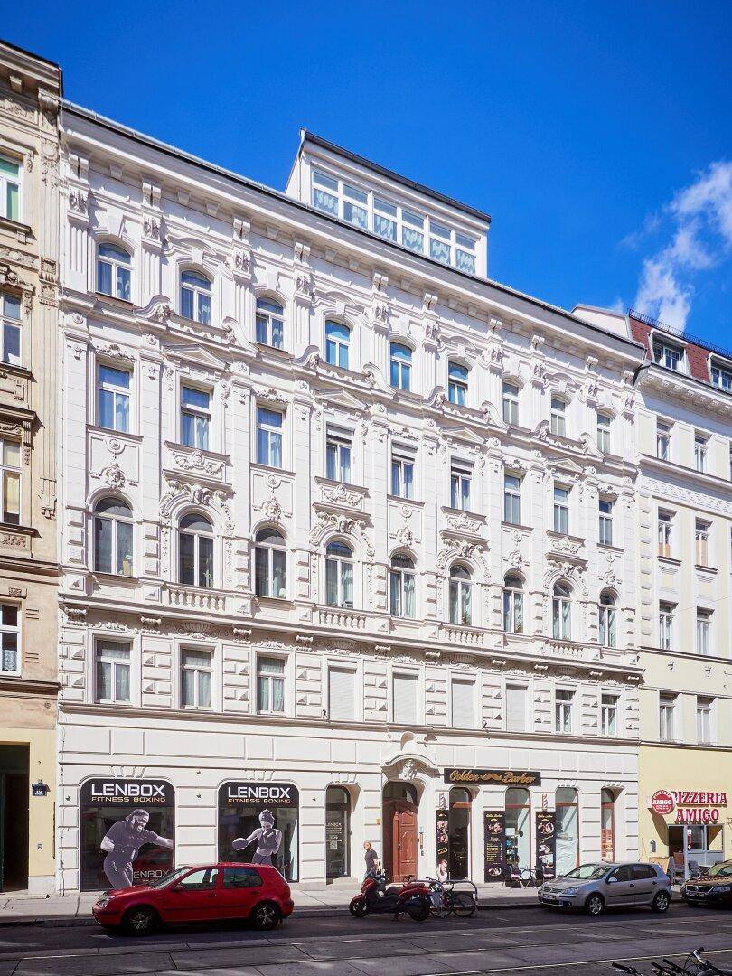 Prunkvolle Altbaufassade mit vielen Fenstern und Geschäften im Erdgeschoss.