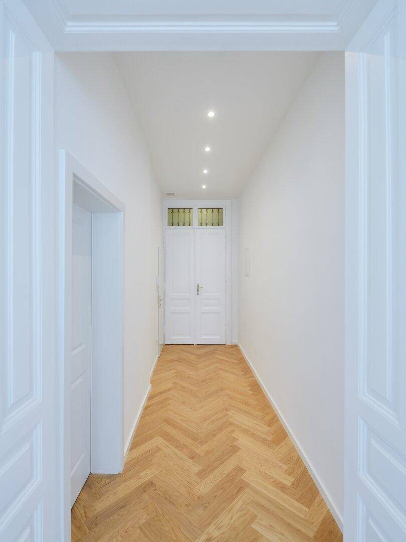 Heller Flur mit Fischgrätparkett und eleganten Doppeltüren, die den Blick in den nächsten Raum freigeben.