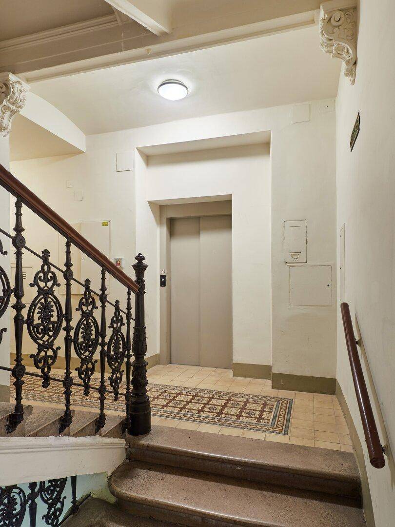 Treppenhaus mit schmiedeeisernem Geländer und modernem Aufzug in einem Altbau.