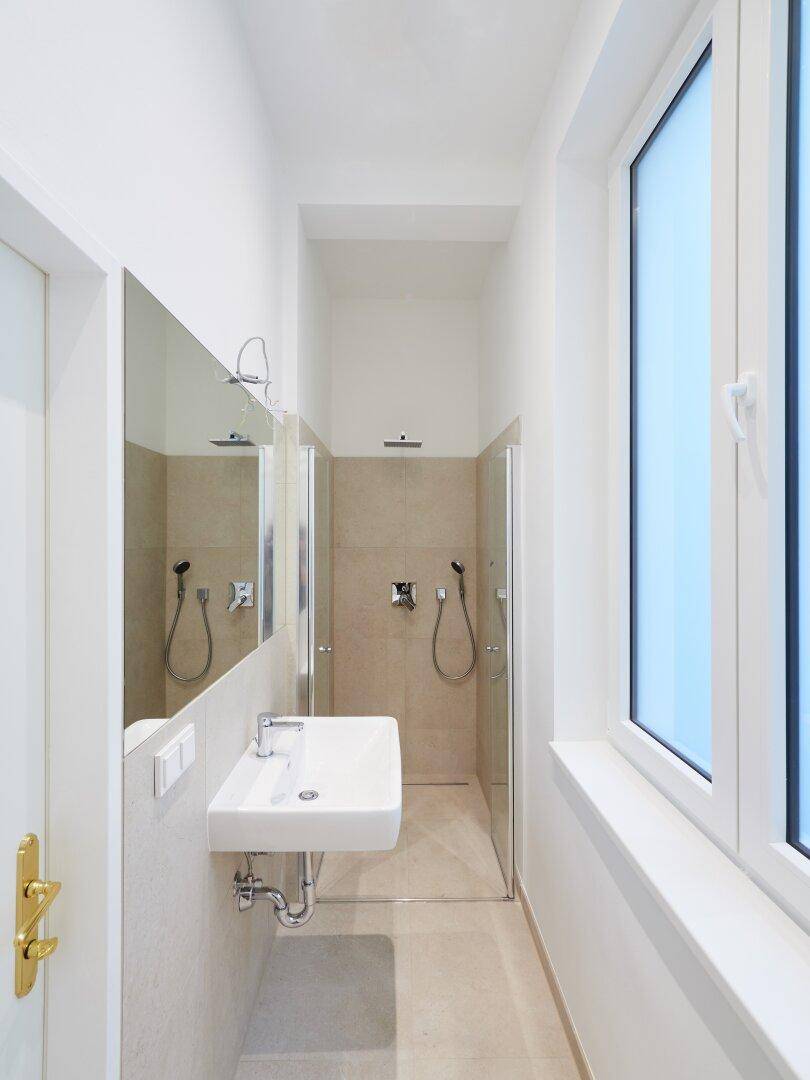Modernes Badezimmer mit begehbarer Dusche, Waschbecken und großem Fenster für Tageslicht.