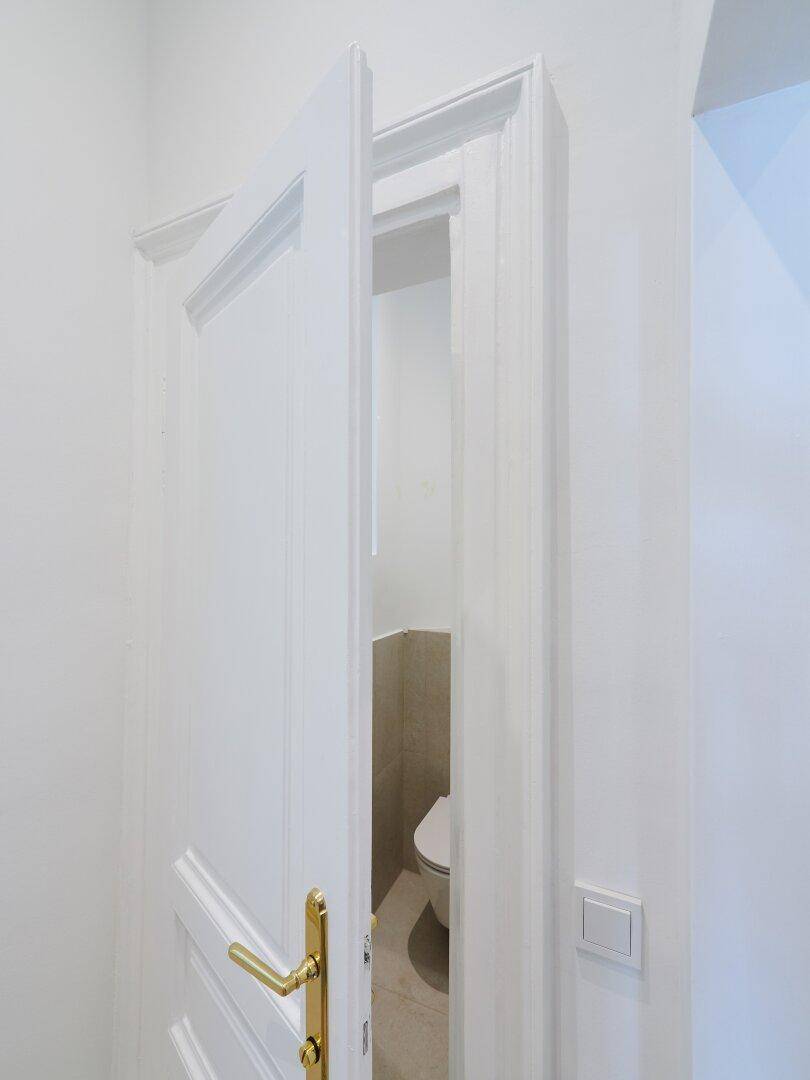 Blick durch eine leicht geöffnete Tür in eine separate Toilette mit modernen Fliesen.