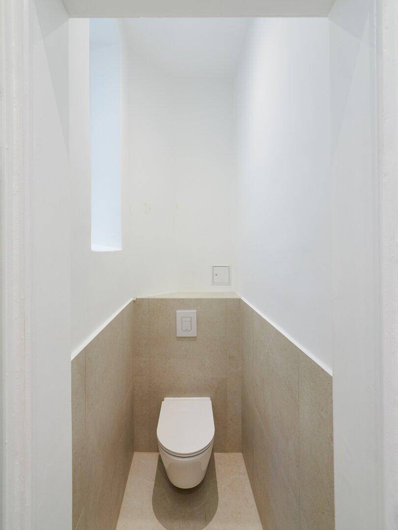 Separate Toilette mit Wand-WC und modernen beigefarbenen Fliesen, minimalistisch gestaltet.