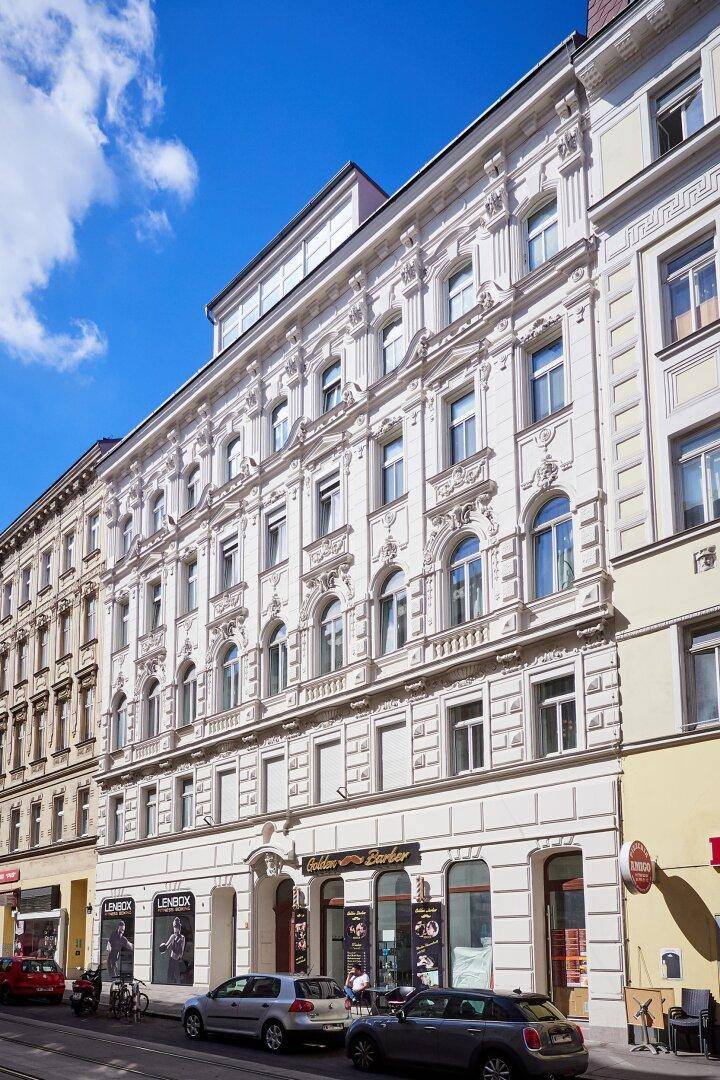 Historische Altbaufassade mit reich verzierten Details und Geschäften im Erdgeschoss.