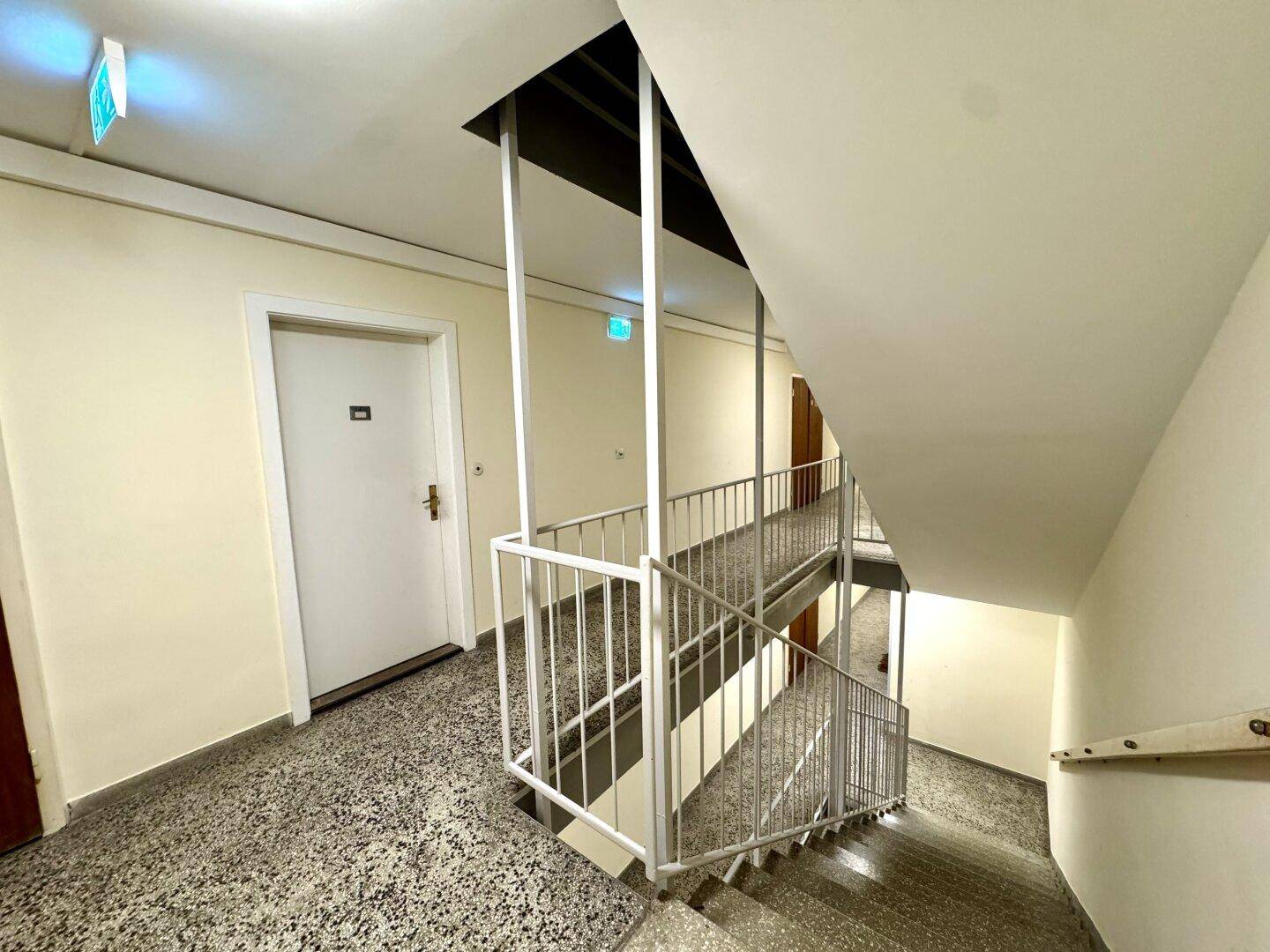 Treppenhaus mit Terrazzoboden und Metallgeländer, das zu den oberen Etagen führt.