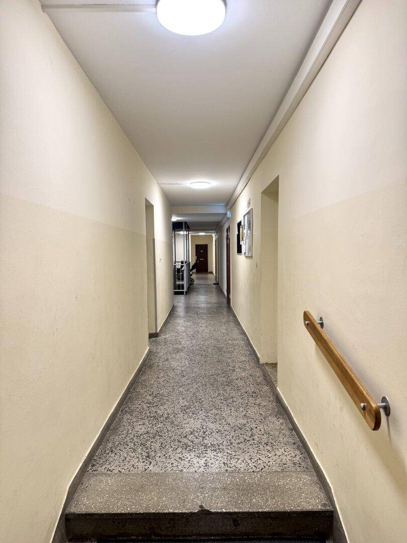Heller Flur mit Terrazzoboden und einem Handlauf, der zu den Wohnungen führt.