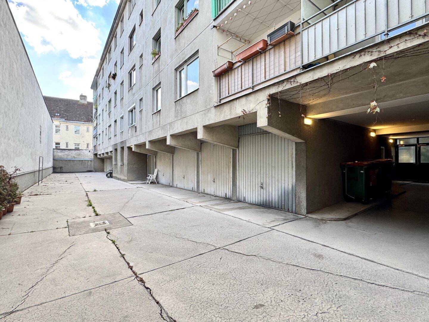 Rückseite eines Wohngebäudes mit Garagen und einem gepflasterten Hofbereich.