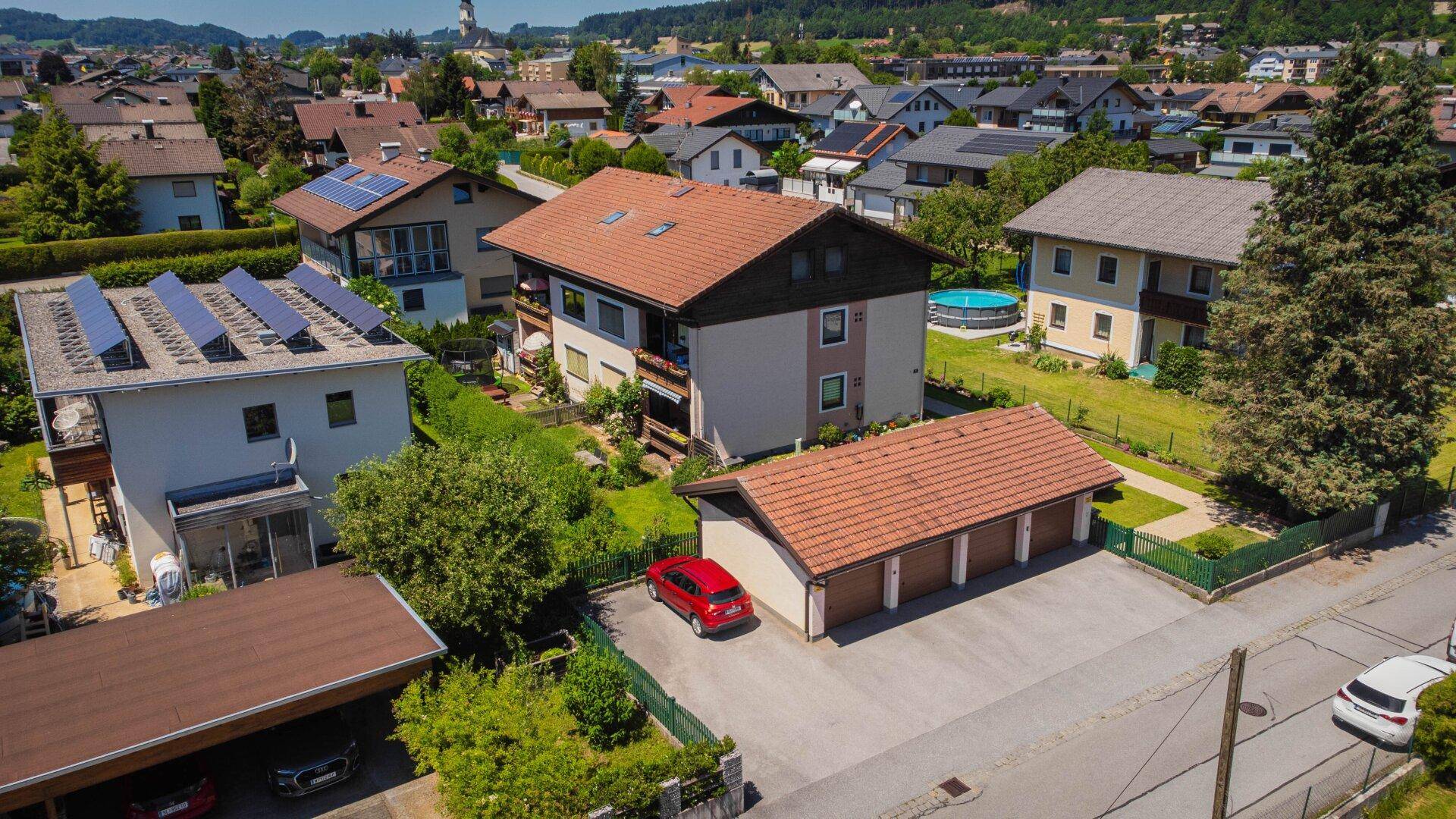 Luftaufnahme eines Wohnhauses mit Garage und umliegenden Gärten in einer sonnigen Wohnsiedlung.