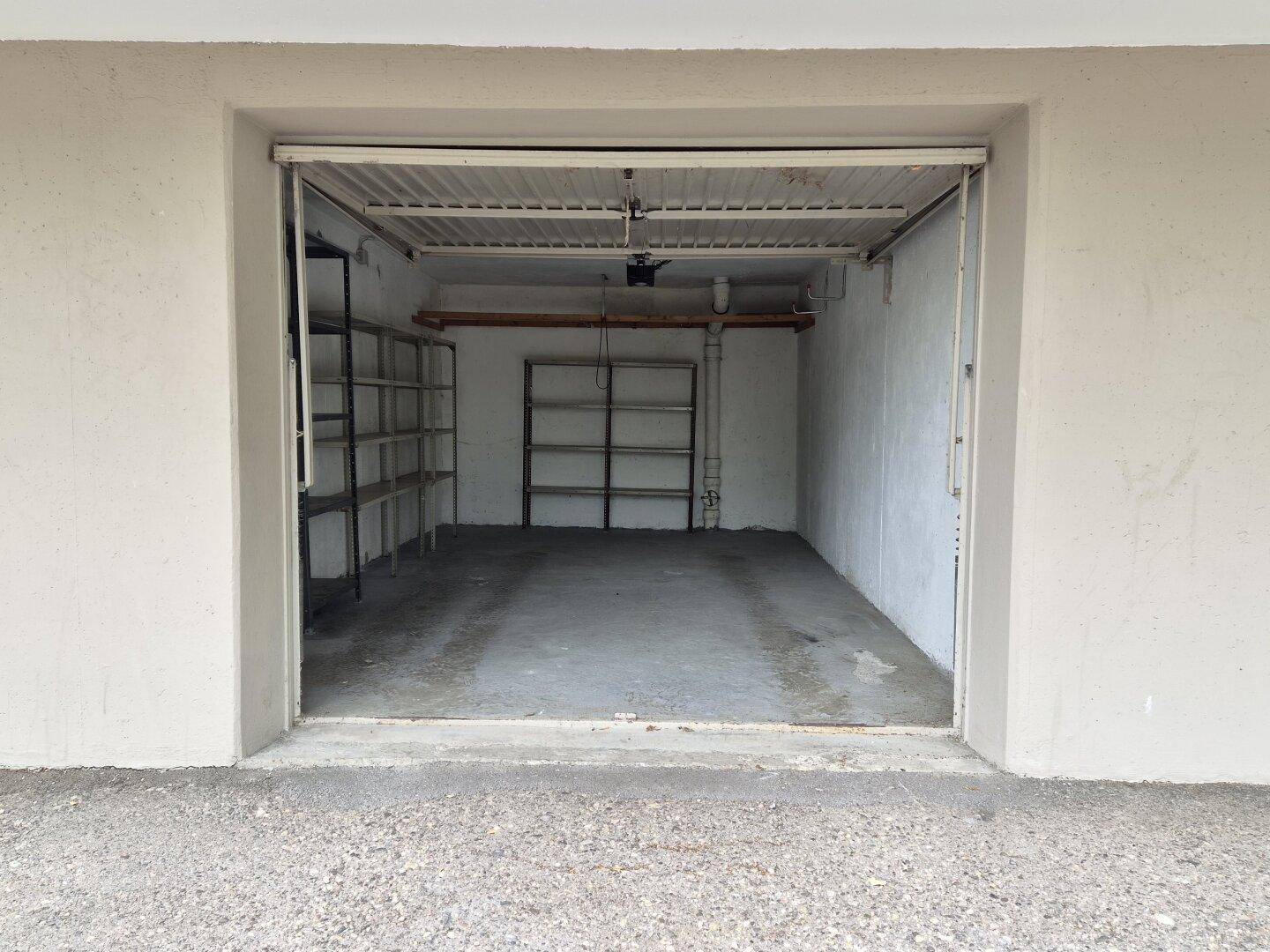 Offene Garageneinfahrt mit Blick auf den Innenraum und die dort installierten Regale.