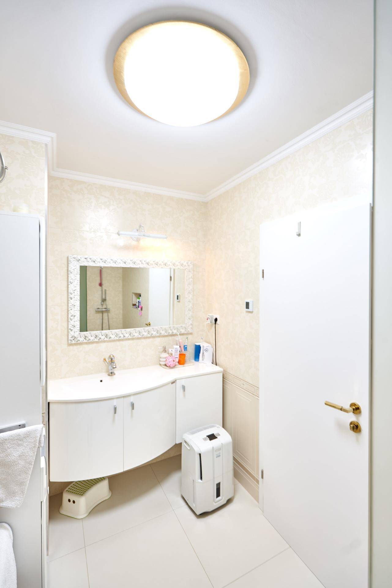 Modernes Badezimmer mit weißem Waschbecken, großem Spiegel und hellen Fliesen an Wänden und Boden.