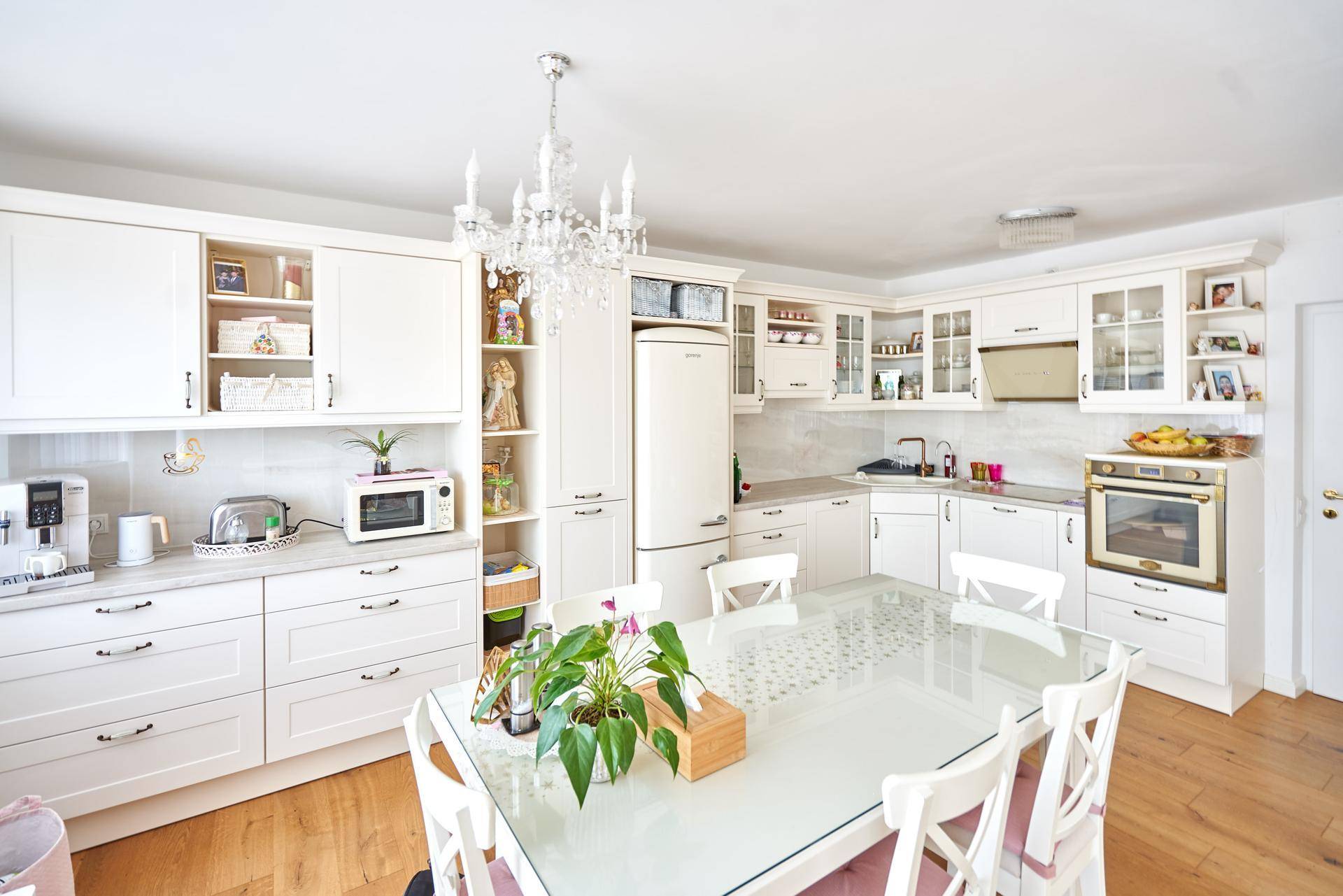 Helle, traditionelle Küche mit weißen Schränken, Holzboden und einem Esstisch in der Mitte.