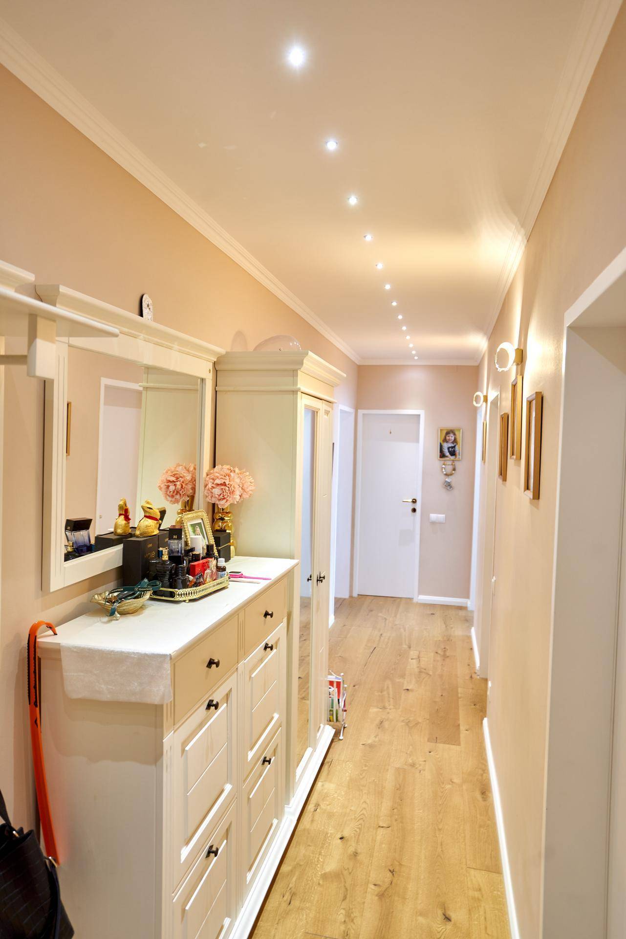 Heller Flur mit Holzboden, Einbauschrank und Spiegel, beleuchtet durch Deckenspots.