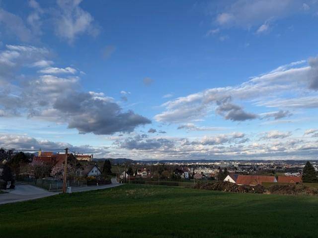 Helles Tageslichtpanorama über ein grünes Feld mit Häusern und der Stadt im Hintergrund.