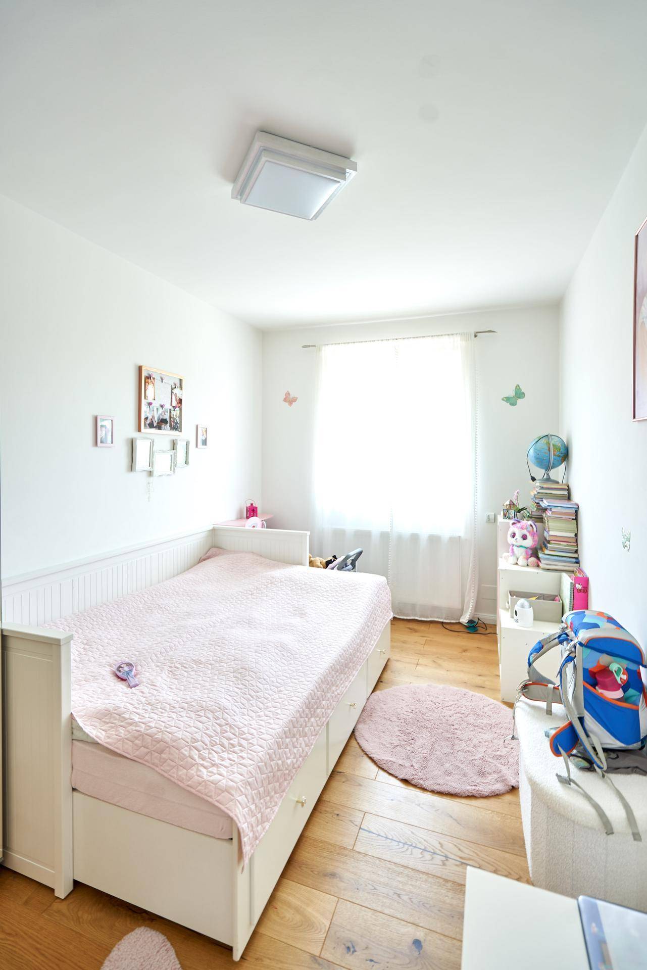 Kinderzimmer mit Einzelbett, Holzboden und einem großen Fenster, das den Raum erhellt.