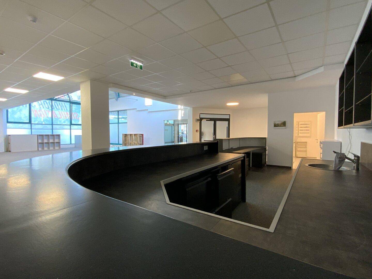Gewerbliche Küchenzeile mit dunklen Arbeitsplatten und Spülbecken in einem offenen Bürobereich.